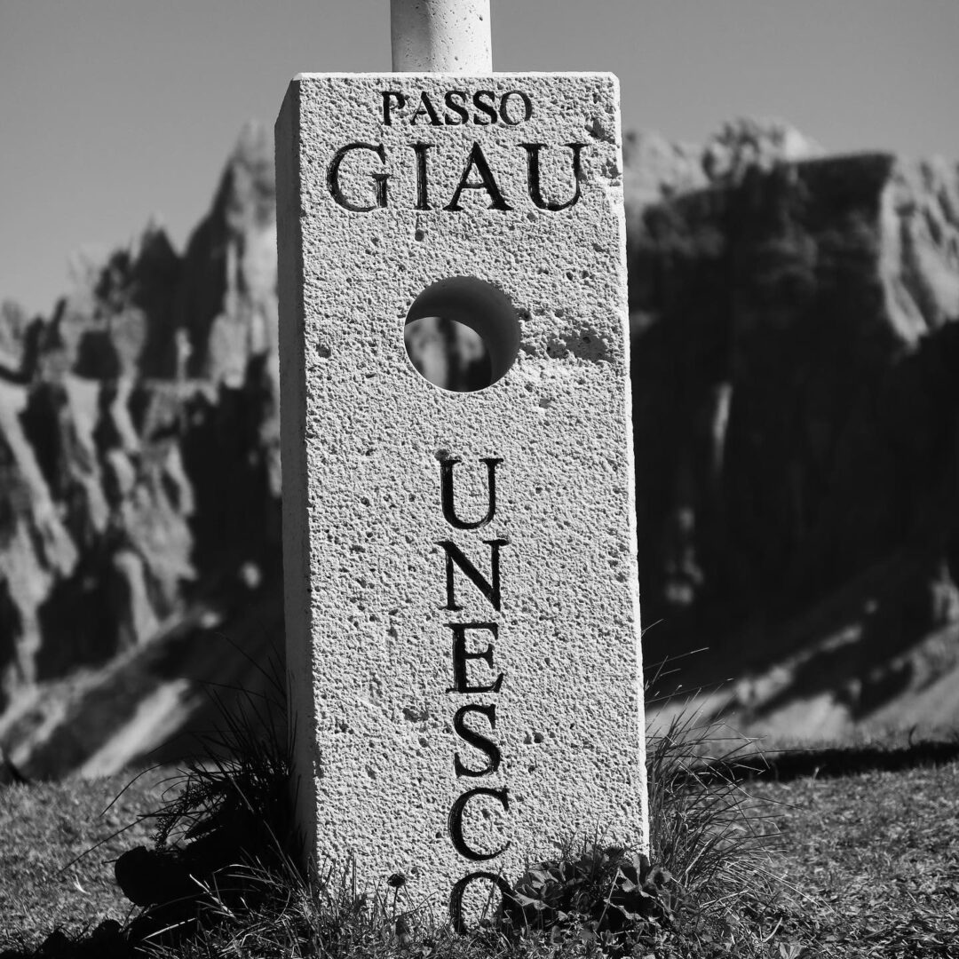 A UNESCO world heritage site marks the summit of Pass Giau, a famous and beautiful road cycling climbing route in Italy's Dolomite mountains. Cycling Passo Giau near Cortina d'Ampezzo in Italy's Dolomites mountains is a rite of passage for road cyclists around the world. Ride Passo di Giau with Alter Exploration on upcoming Secret Dolomites cycling tours.